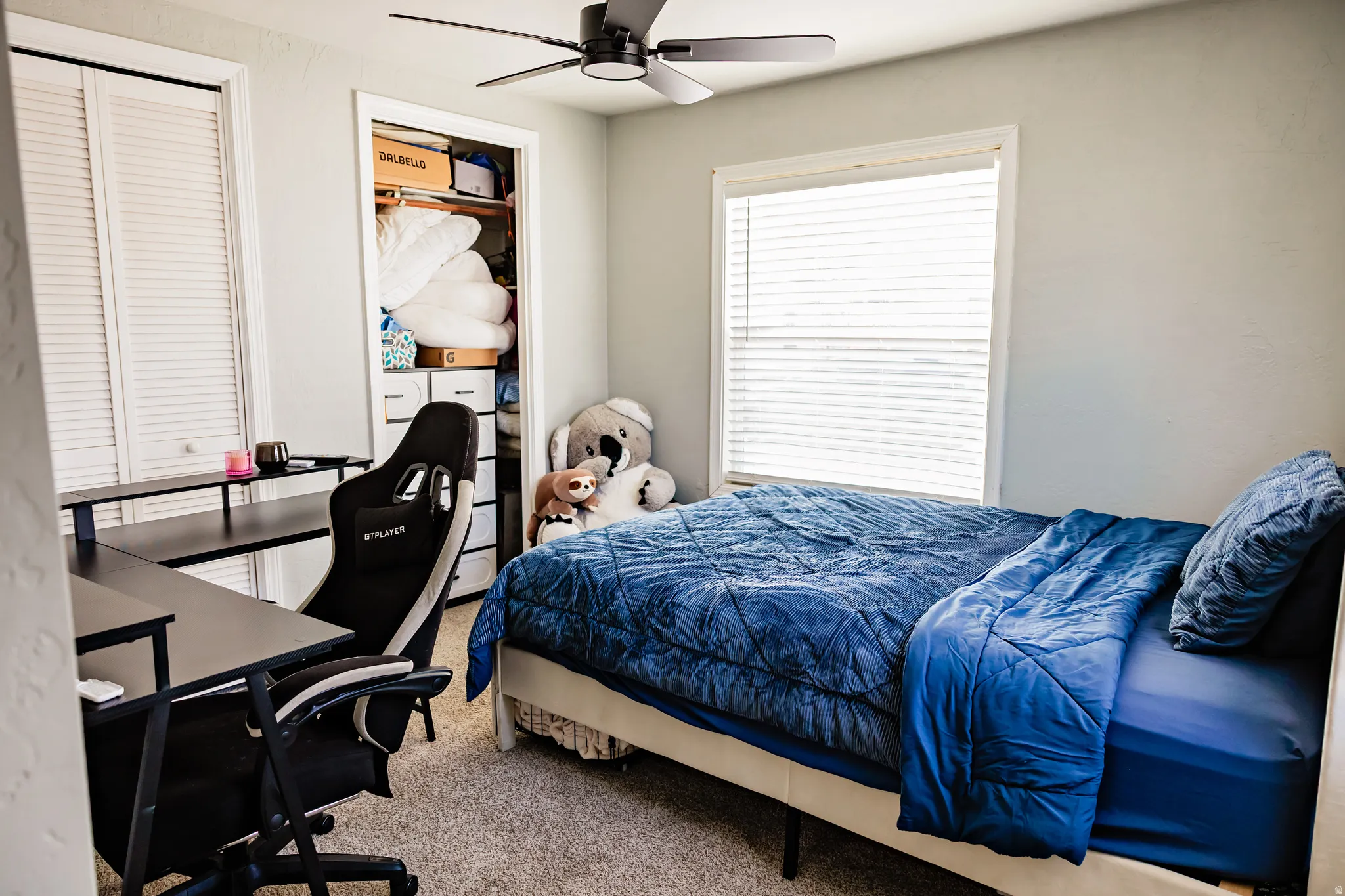 Recessed closet with built-in shelving, window with blinds, and ceiling fan