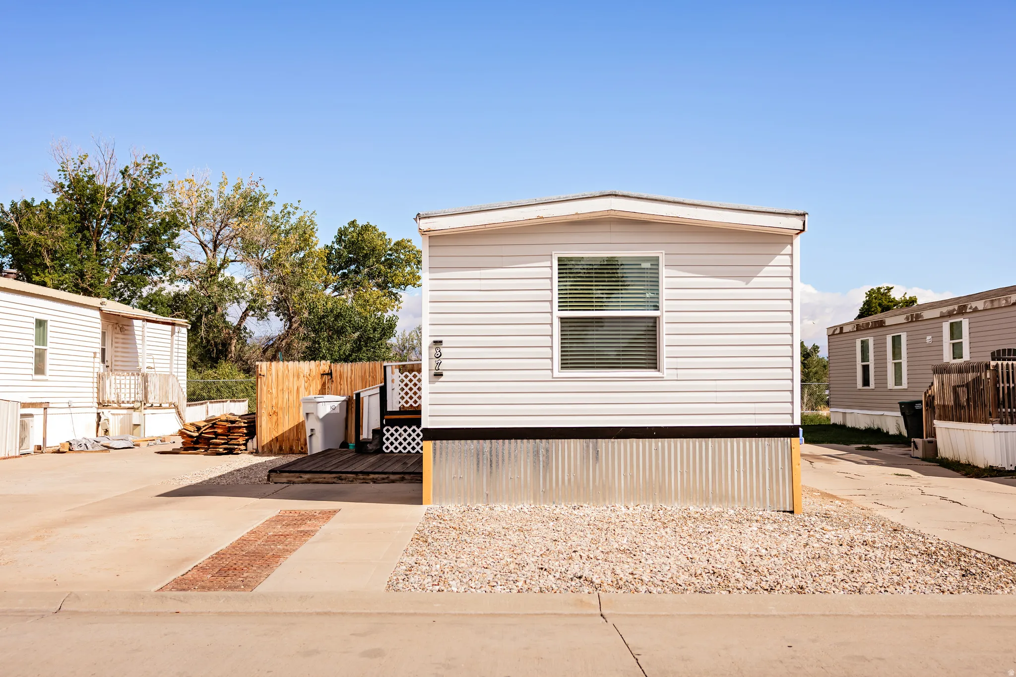 White horizontal siding exterior with a single window, gravel landscaping, and a wooden deck entry