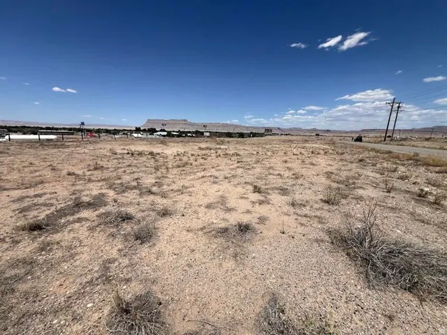 Expansive arid landscape featuring a clear sky, distant mesa formations, and a paved road with utility poles
