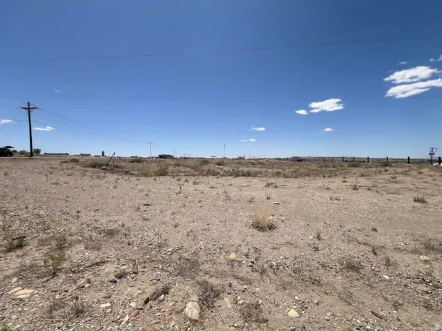Expansive undeveloped land featuring a clear sky, distant power lines, and a section of fence posts