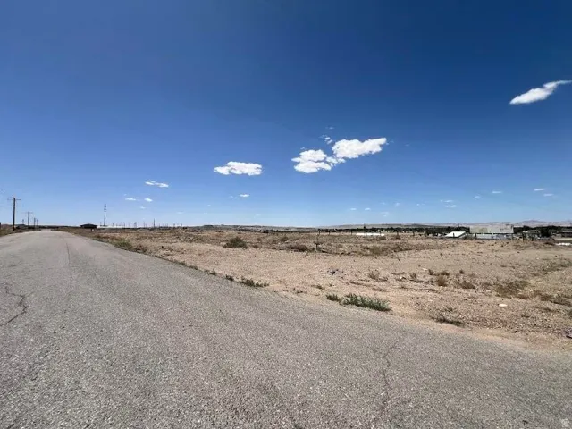 Sprawling land parcel featuring a paved road, distant structures, and open sky