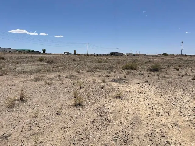 Expansive undeveloped land parcel featuring scattered vegetation and a clear sky backdrop