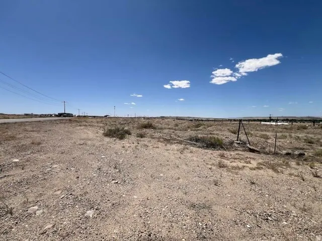 Expansive parcel featuring a gravel and dirt surface, sparse natural vegetation, and utility lines present at the property boundary