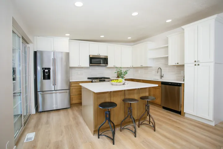 Gourmet kitchen with wood-finish flooring, white shaker cabinetry, stainless steel appliances, a center island with countertop seating, and a tile backsplash