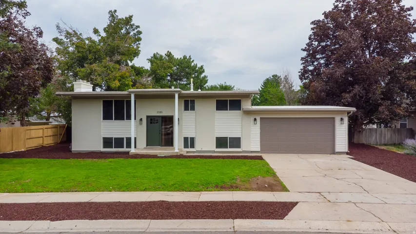 Split-level residence featuring a two-car garage, manicured lawn, and a fenced backyard