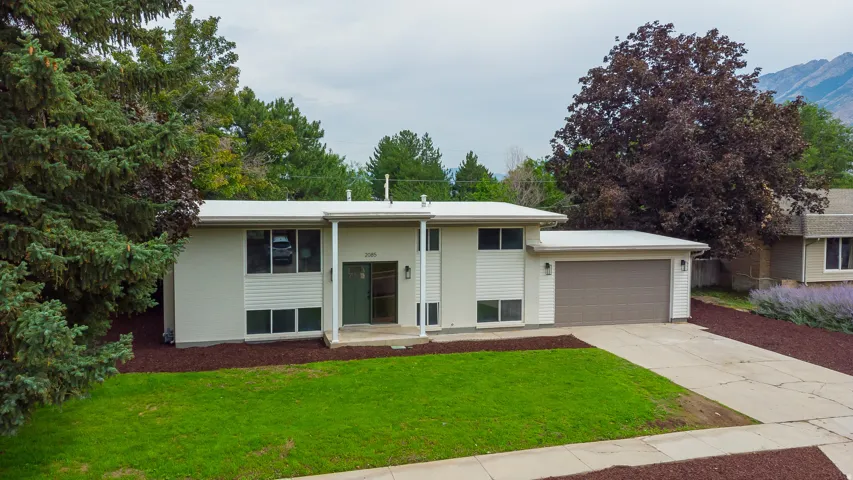 Split-level residence featuring a two-car garage, concrete driveway, and mature landscaping