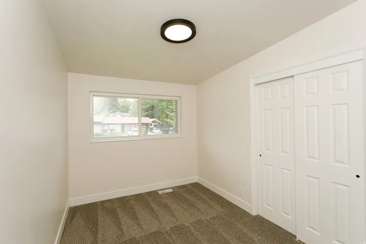 Neutral wall paint, textured carpeting, a flush mount ceiling light fixture, and a sliding door closet with panel detailing
