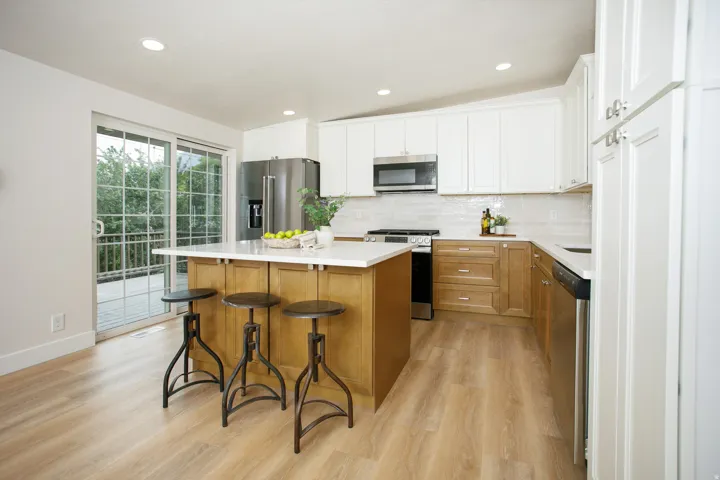 Kitchen featuring a central island, white shaker-style upper cabinetry, wood-finish lower cabinetry, and stainless steel appliances