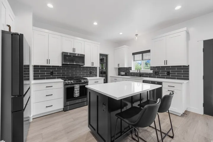 Contemporary kitchen featuring white cabinetry, black subway tile backsplash, stainless steel appliances, and a central island with a solid surface countertop