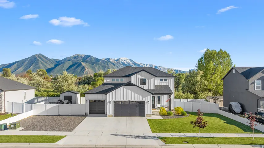 Modern exterior featuring vertical siding, attached two-car garage, manicured lawn, paved driveway, and mountain backdrop