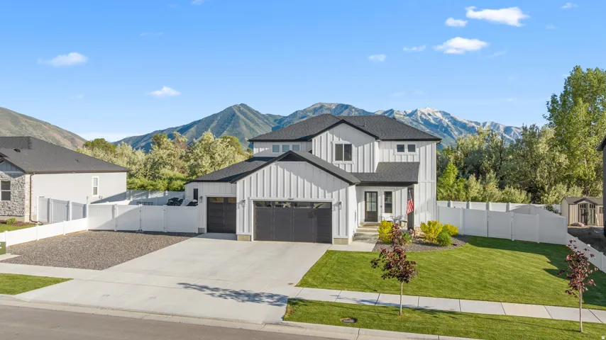 Modern farmhouse-style exterior with black-framed windows, a two-car garage, manicured lawn, and a white privacy fence