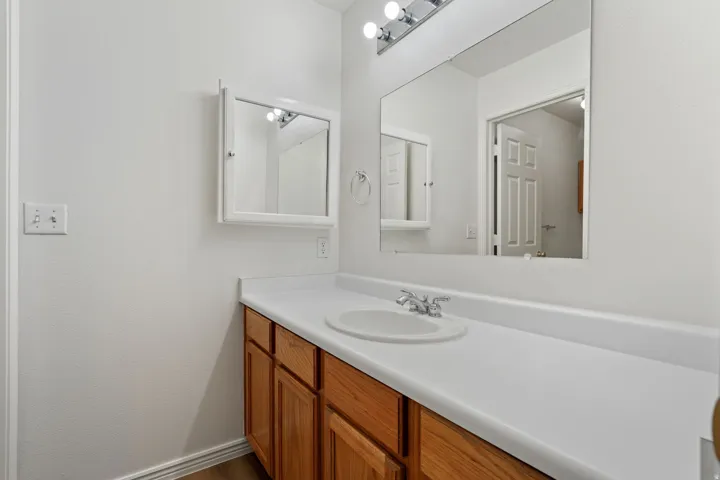 Wood-finish flooring with a white vanity featuring a laminate countertop, an integrated sink, and an expansive wall mirror