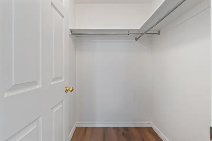 Wardrobe closet featuring wood-finish flooring, white walls, and built-in shelving with hanging rods