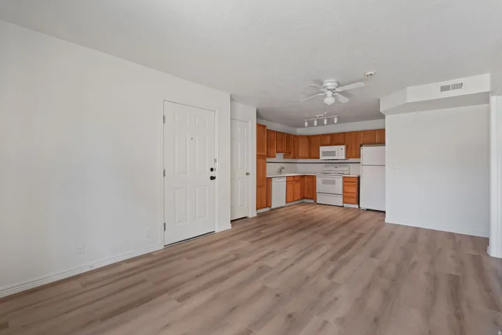 Wood-finish flooring, white walls, kitchen with wood cabinetry, white appliances, and a ceiling fan