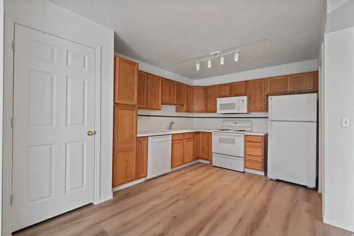 Kitchen featuring wood-finish flooring, wood cabinetry, white appliances, white countertops, and white subway tile backsplash