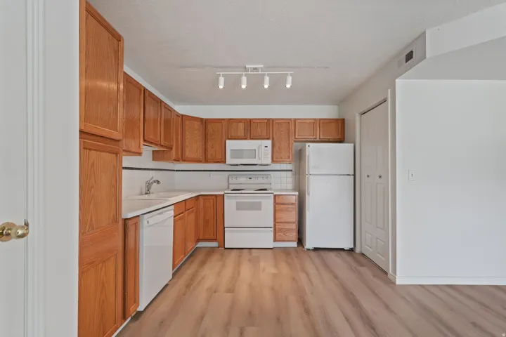 Kitchen featuring wood-finish cabinetry, white appliances, white tile backsplash, and wood-look flooring