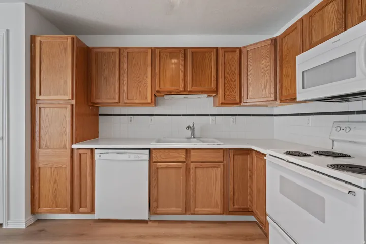 Kitchen featuring wood-finish cabinetry, white countertops, white tile backsplash with black trim, and a full suite of white appliances including a built-in microwave and dishwasher