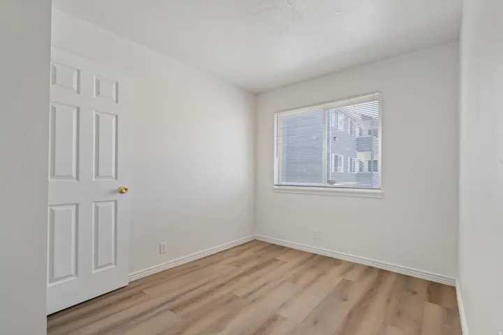 Neutral wall paint, wood-finish flooring, white trim, and a window with blinds