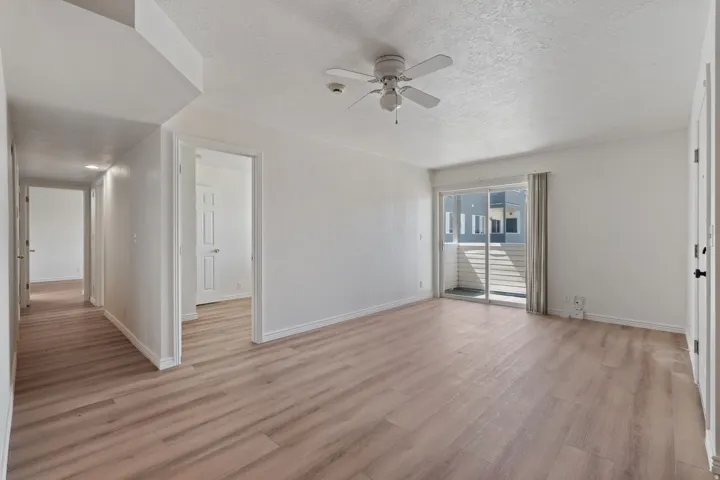Spacious living area featuring wood-finish flooring, a ceiling fan, and sliding glass doors opening to a balcony