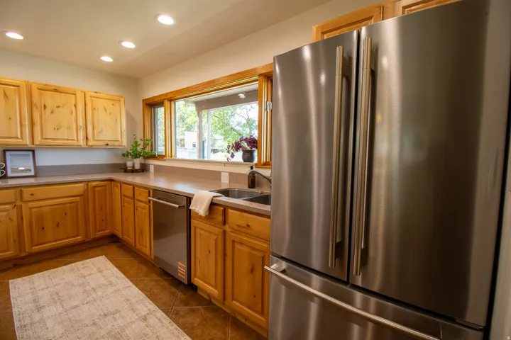 Custom wood cabinetry, stainless steel appliances, dual basin sink, light-toned countertops, and recessed lighting