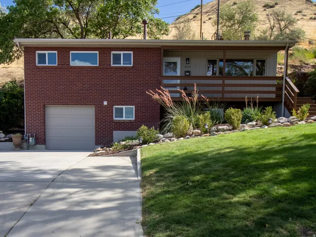 Brick facade with a neutral-toned garage door, wood-paneled balcony, and a manicured lawn
