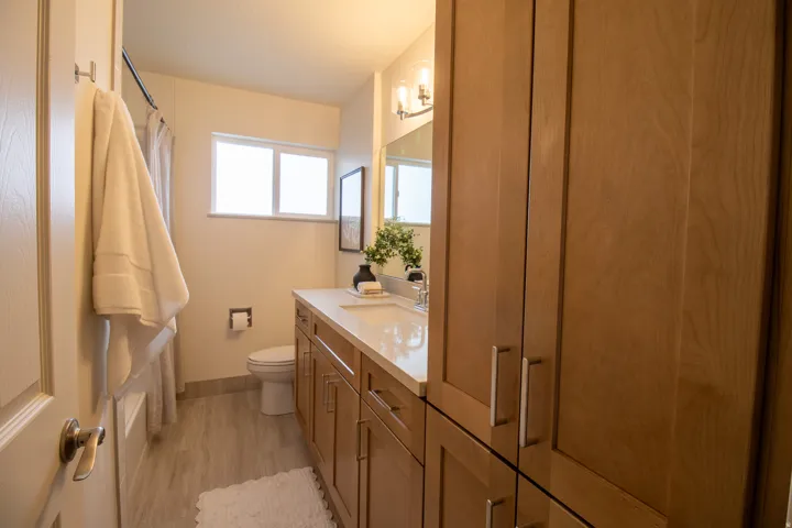 Bathroom featuring a light wood-finish vanity with an integrated sink and light countertop, complementing tall storage cabinetry, a toilet, and a window