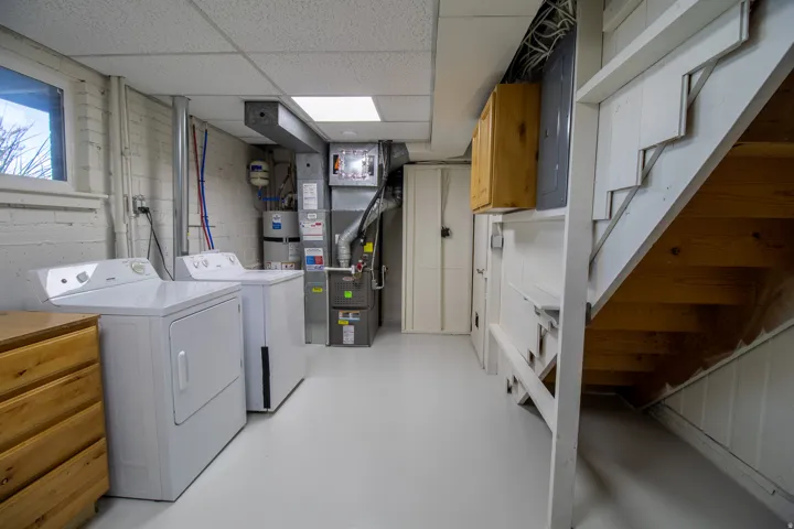 Laundry area with white appliances, light-colored flooring, and exposed mechanical systems