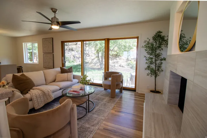 Hardwood flooring, sliding glass door, white walls, ceiling fan with integrated lighting, and a tiled fireplace
