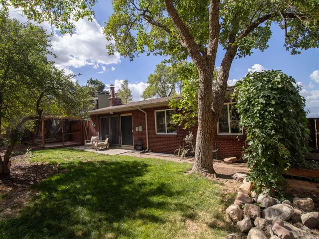 Expansive backyard featuring a manicured lawn, established shade trees, a brick exterior, and a built-in deck