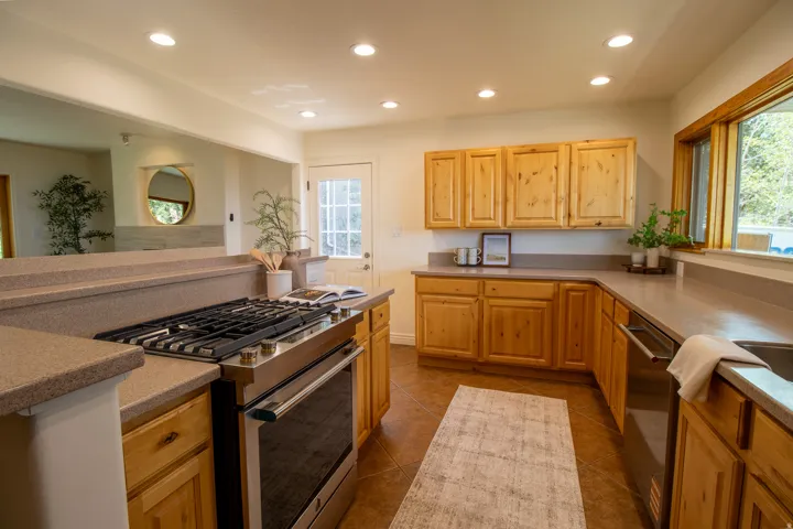 Hardwood cabinetry with stainless steel appliances, recessed lighting, tile flooring, and a large window