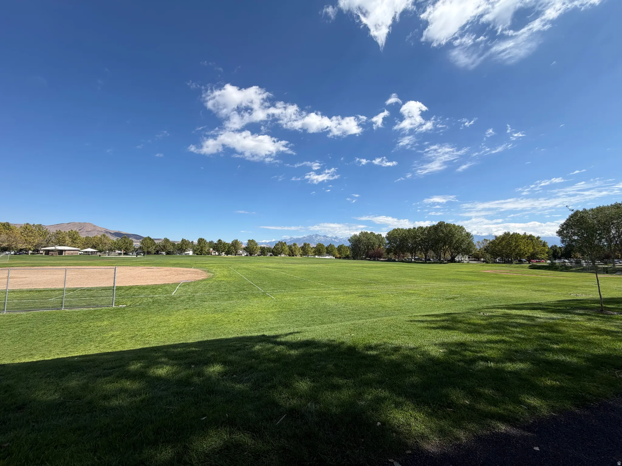 Expansive green field with a baseball diamond, surrounded by mature trees and mountain scenery