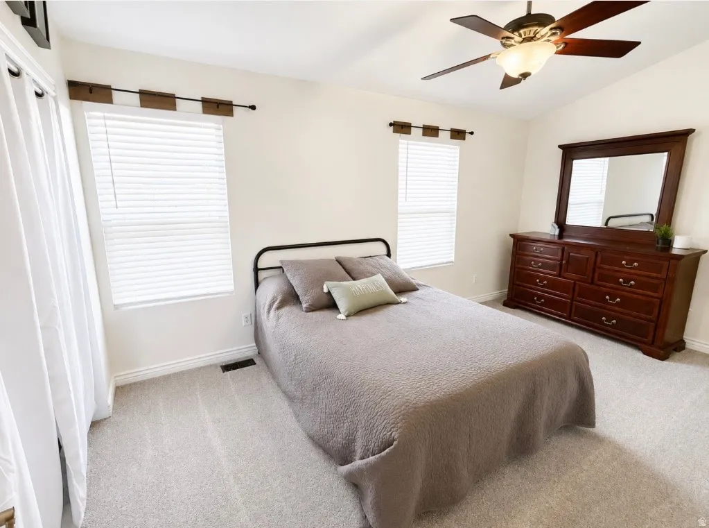 Light-colored carpet flooring, two windows with blinds, and a ceiling fan with integrated lighting