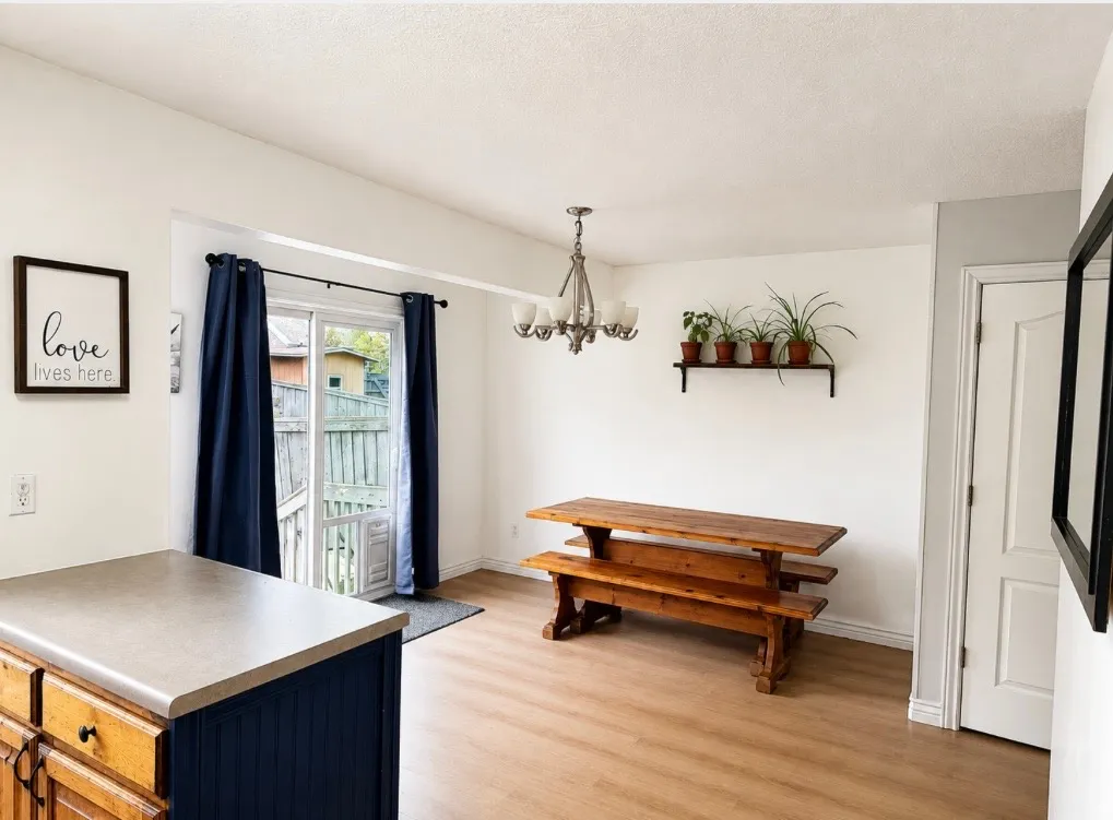 Light wood-finish flooring, sliding glass door leading to outdoor space, built-in wall shelving, kitchen island with contrasting cabinetry, and a ceiling-mounted chandelier
