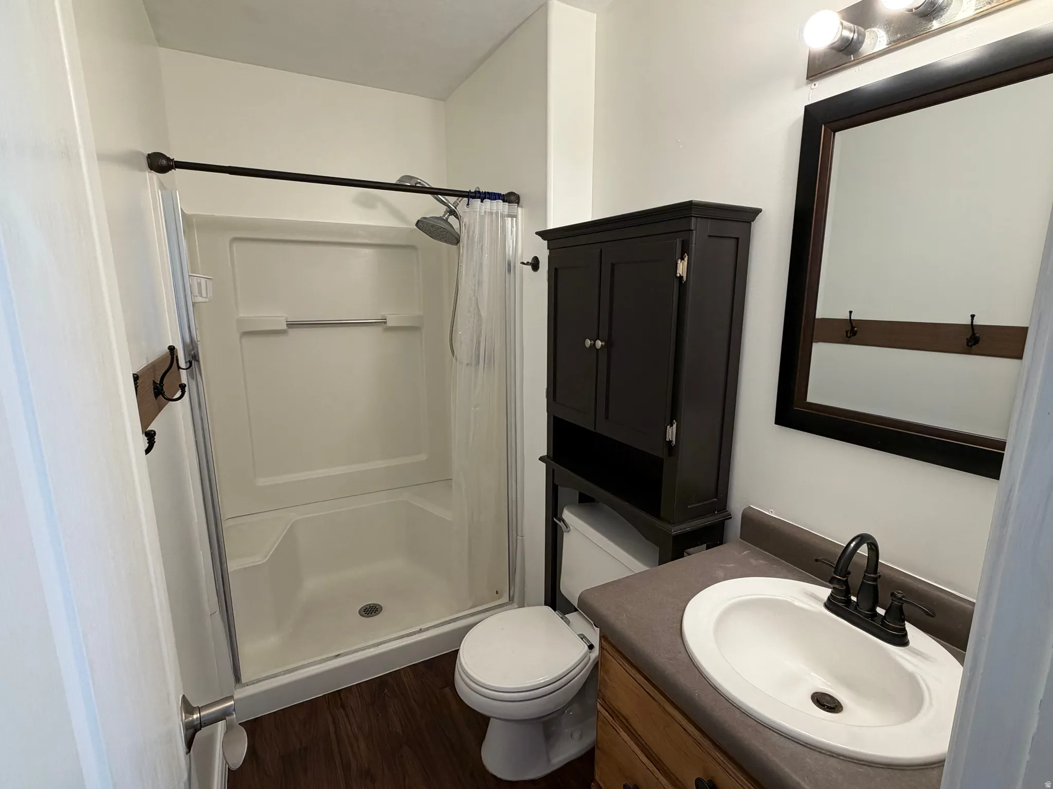 Wood-finish flooring with a vanity featuring a white oval sink and black faucet