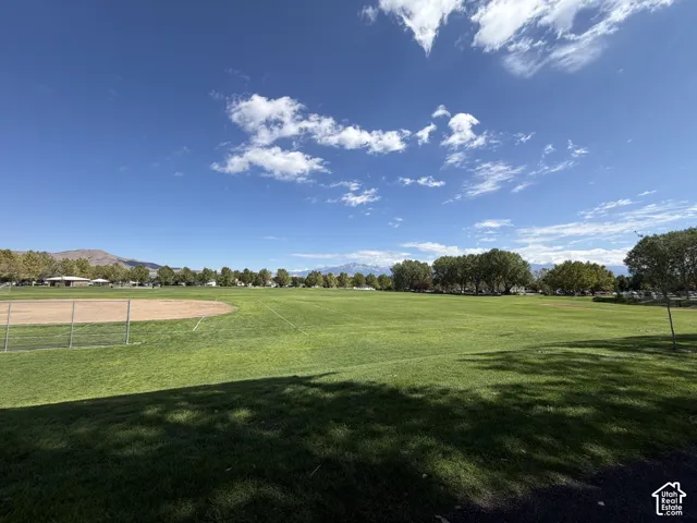 Expansive green field with a baseball diamond, surrounded by mature trees and mountain scenery