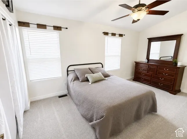 Light-colored carpet flooring, two windows with blinds, and a ceiling fan with integrated lighting