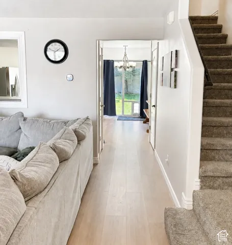 Light wood-finish flooring extending through the hallway, carpeted stairs with a dark handrail, and a contemporary chandelier visible through the doorway