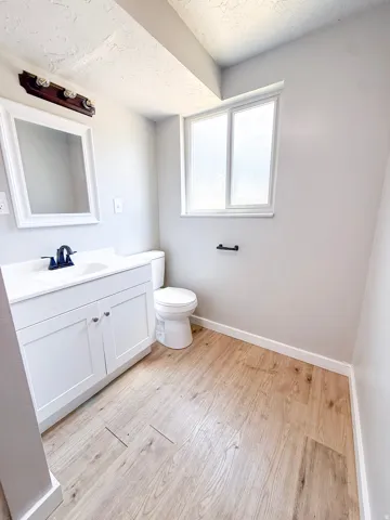 White vanity with dual cabinet storage, white framed mirror, and wood-finish flooring