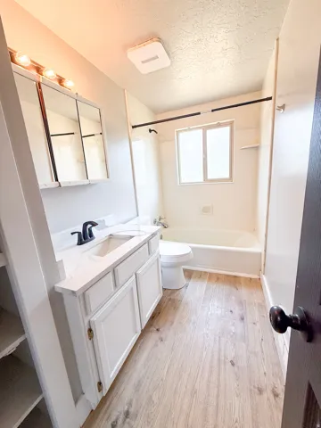 Bathroom featuring a white vanity with integrated sink, matte black faucet, and wood-finish flooring