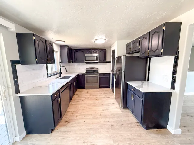 U-shaped kitchen featuring black cabinetry, light-toned countertops, white subway tile backsplash, and wood-finish flooring