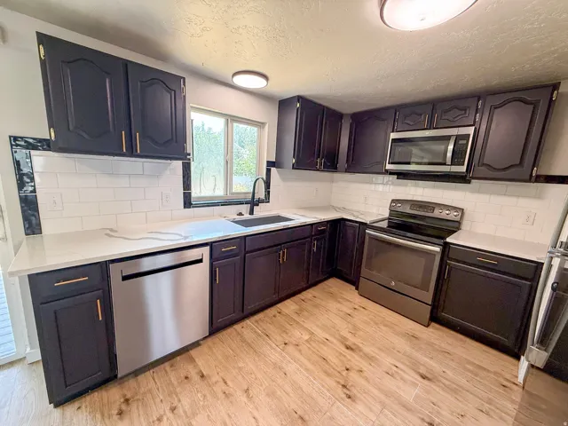 Kitchen featuring dark wood-finish cabinetry, stainless steel appliances, white subway tile backsplash, light-toned countertops, and wood-finish flooring