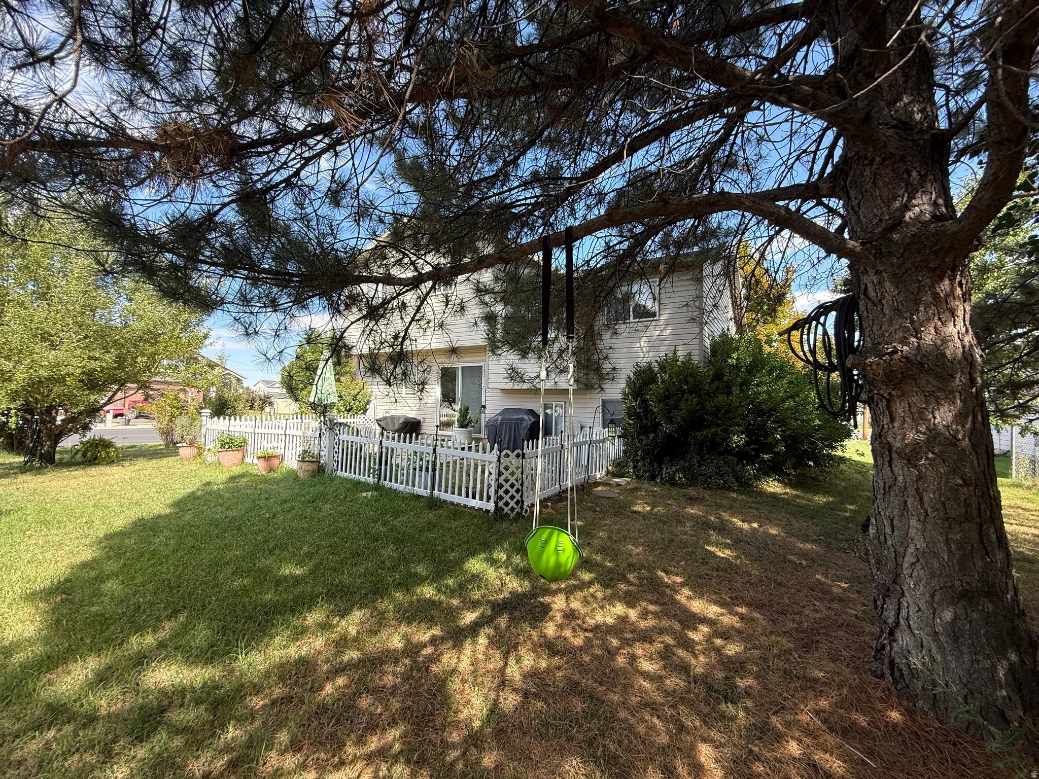 Expansive backyard featuring a manicured lawn, established shade trees, a white picket fence, and a patio with a sliding glass door entry