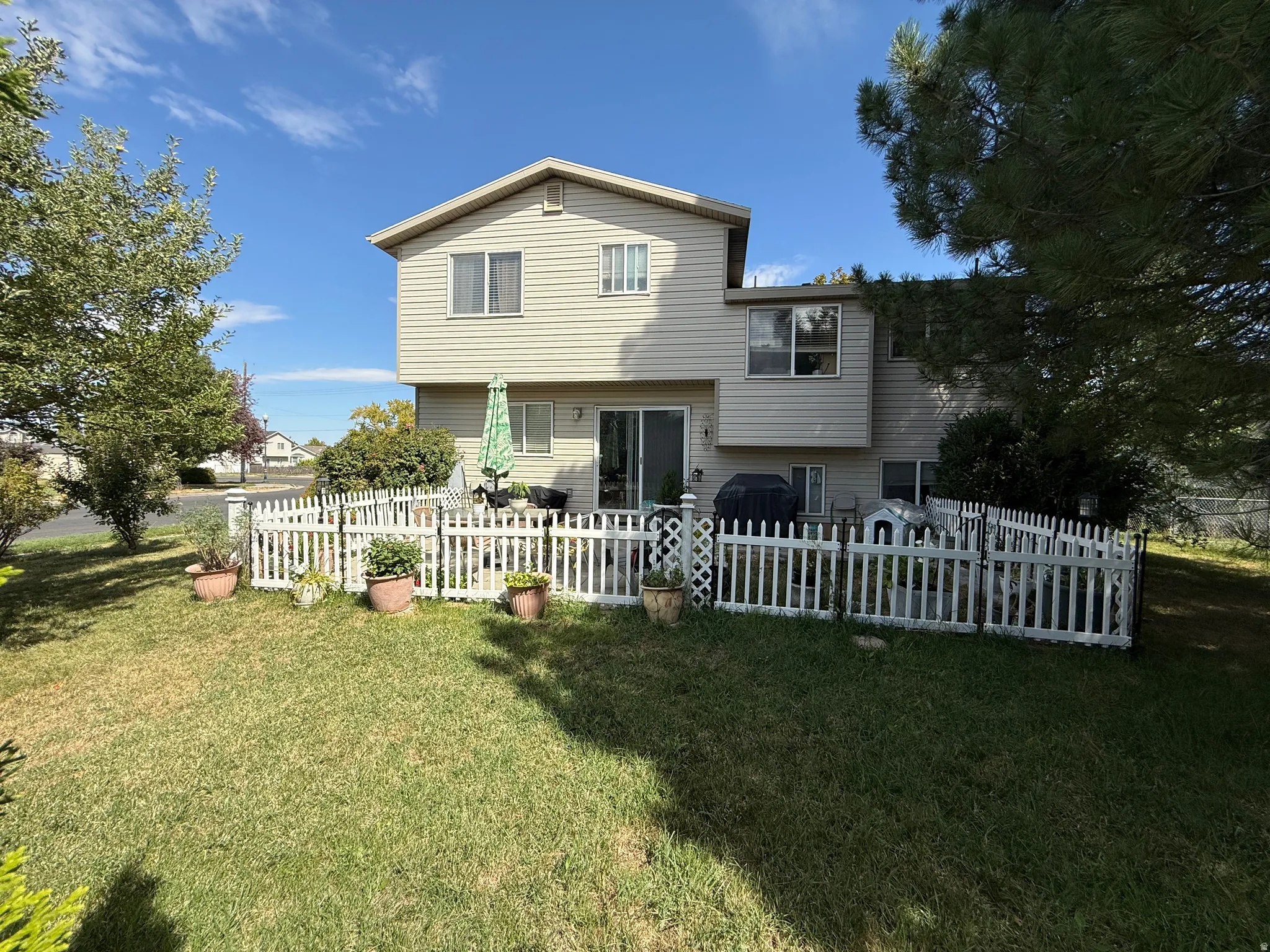 Rear exterior featuring horizontal siding, a sliding glass patio door, a white picket fence, and a manicured lawn