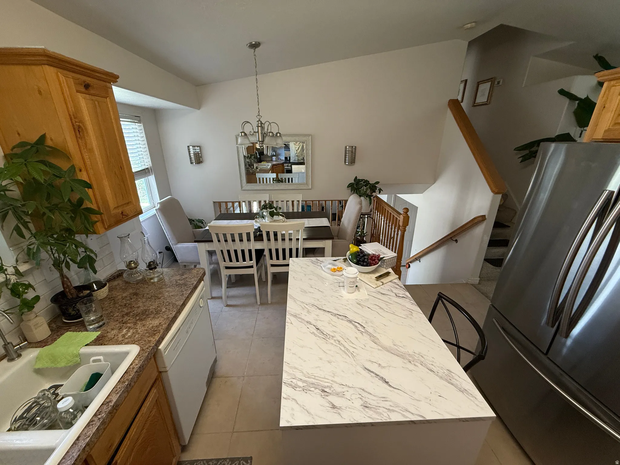 Kitchen island with a light-toned, veined countertop, stainless steel refrigerator, and wood-finish cabinetry
