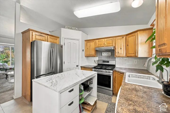 Kitchen featuring wood cabinetry, stainless steel appliances, a white subway tile backsplash, and a central island with a light-colored countertop