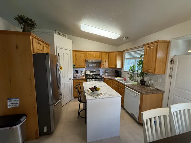 Kitchen featuring wood-finish cabinetry, a central island with a light-toned countertop, a stainless steel refrigerator, and a gas range