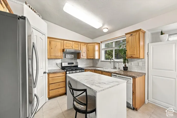 Kitchen featuring a center island with a stone-finish countertop, wood cabinetry, stainless steel appliances, and a tile backsplash