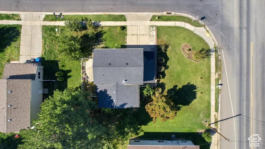 Corner lot property with a dark shingle roof, mature landscaping, and concrete sidewalks