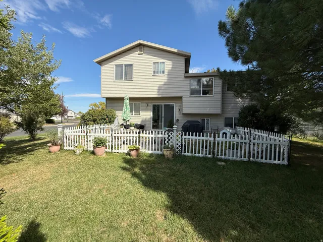 Rear exterior featuring horizontal siding, a sliding glass patio door, a white picket fence, and a manicured lawn
