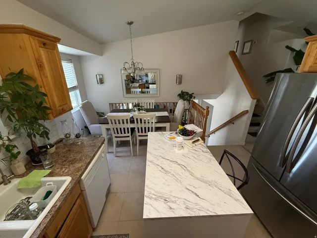 Kitchen island with a light-toned, veined countertop, stainless steel refrigerator, and wood-finish cabinetry